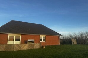 A single-story brick house with a sloped roof, a fenced yard, and a clear sky. - Holiday home in the North Sea with 2 bedrooms (Westerhever)