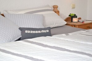 A neatly made bed with a grey pillow and a white pillow with a striped pattern. - Möhring Holiday Farm (Warwerort)