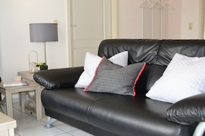A black leather sofa with three pillows, a small table with a lamp, and a door in the background. - Möhring Holiday Farm (Warwerort)