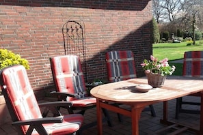 An outdoor patio with a round wooden table and two chairs with plaid upholstery. - Holiday home in Dunum with swimming pool (Dunum)