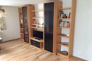 A room with a wooden floor, built-in shelving units, a television, and a lamp. - Holiday home in Dunum with swimming pool (Dunum)