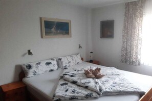 A bedroom with a bed, a nightstand, a wall-mounted lamp, and a window with curtains. - Holiday apartment with 2 bedrooms (Bodensdorf)