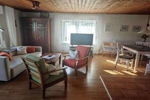 Ein Wohnzimmer mit einer Couch, Sesseln, einem Esstisch und einem Fernseher.