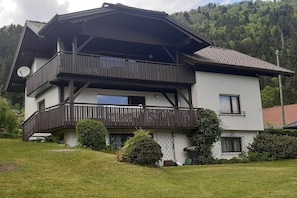 A two-story building with a balcony, surrounded by greenery and hills. - Holiday apartment with 2 bedrooms (Bodensdorf)