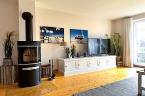 A living room with a wood-burning stove, white cabinets, a flat-screen TV, and two framed pictures on the wall. - Holiday apartment with 2 bedrooms (St. Peter-Ording)