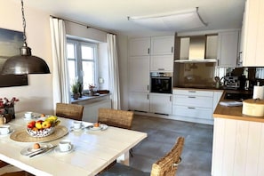 Une cuisine moderne avec des meubles blancs, une table à manger dressée avec des assiettes, des tasses et un panier de fruits.