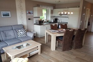 Een knus woongedeelte met een bank, een eettafel met stoelen, een keukenhoek en een kleine salontafel.