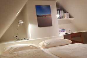 A bedroom with a bed, a desk, a chair, a lamp, and a bookshelf. - Witthüs holiday apartment 16 (Wenningstedt)