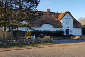 Ein traditionelles Gebäude mit einem Reetdach, einer Steinmauer und einem Holzzaun.