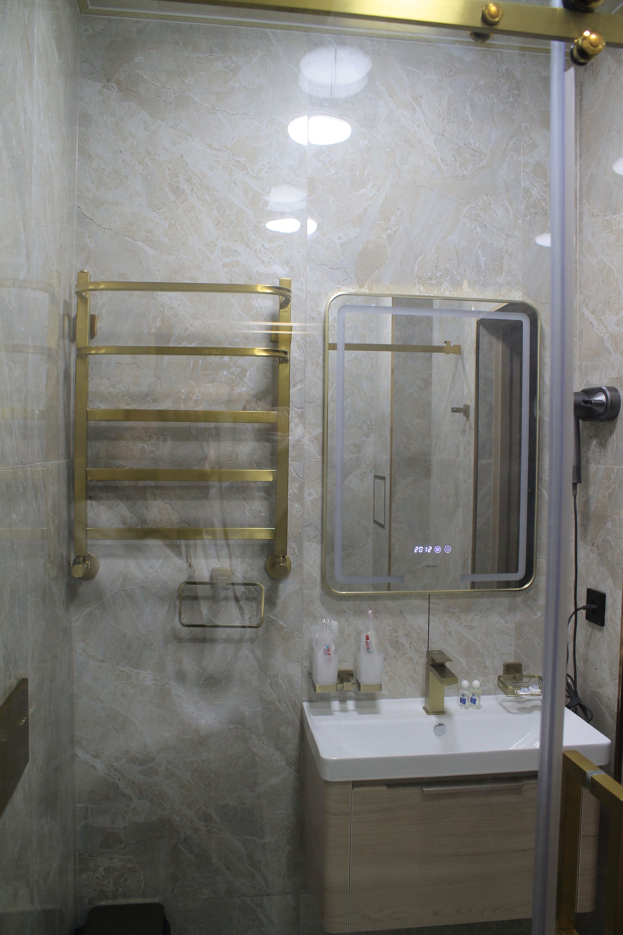 Une salle de bain avec un mur en marbre, un porte-serviettes doré, un miroir et un lavabo avec des articles de toilette.