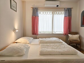 A bedroom with a bed, two pillows, a chair, a window with curtains, and a wall-mounted light. - Ok36 Holiday Home With dog Oostkapelle (Oostkapelle)