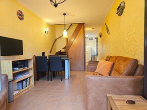 Ein Wohnzimmer mit einer Couch, einem Fernseher, einem Bücherregal und einem Essbereich mit Stühlen und einem Tisch.
