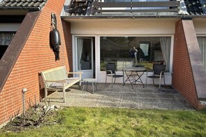 Eine Terrasse mit Tisch, Stühlen und einer Bank, sowie einer hängenden Dekoration.