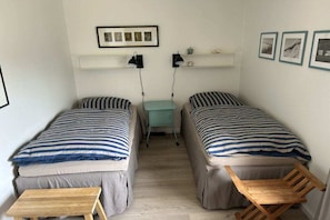Ein kleines, gemütliches Zimmer mit zwei Einzelbetten, einem kleinen Tisch und einem Regal mit Bildern.