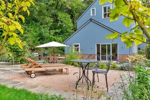 A patio with a table and chairs, a wooden lounge chair, and a covered umbrella. - The Blue Barn (Tunbridge Wells)