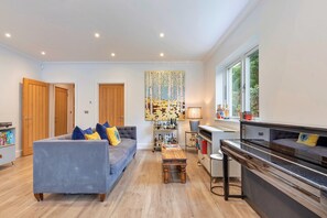 A modern living room with a sofa, a coffee table, a piano, and a bookshelf. - The Blue Barn (Tunbridge Wells)