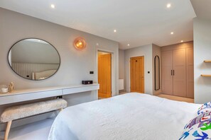 Une chambre avec un grand lit, un miroir rond, une table de chevet, un banc, une armoire et une porte.