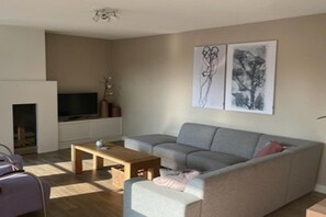 A modern living room with a grey sofa, a coffee table, and a flat-screen TV mounted on the wall. - Luxury holiday home on Ameland (Nes)