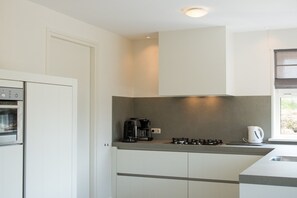 A modern kitchen with a built-in oven, a coffee maker, and a kettle on the counter. - Luxury holiday home on Ameland (Nes)