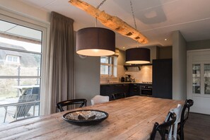 A modern kitchen with a wooden dining table, pendant lights, and a view of the outdoors. - Luxury dune villa on Ameland (Nes)