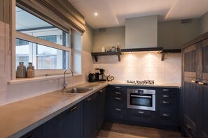 A modern kitchen with a built-in oven, stainless steel appliances, and a window with a view. - Luxury dune villa on Ameland (Nes)