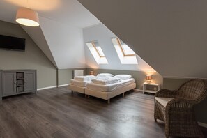 A bedroom with a sloped ceiling, a bed, a chair, and a television. - Luxury dune villa on Ameland (Nes)