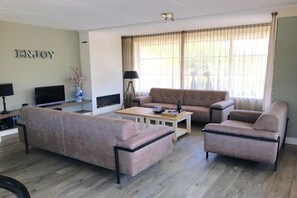 A living room with a sofa, armchairs, a coffee table, a TV, and a fireplace. - Luxury dune villa on Ameland (Nes)