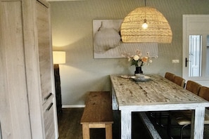 A dining area with a rustic wooden table, a bench, a hanging light fixture, and a wall-mounted artwork. - Charming villa in the dunes of Ameland (Nes)