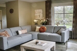 Ein Wohnzimmer mit einem grauen Ecksofa, einem Couchtisch und einem Fenster mit Vorhängen.