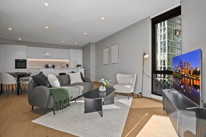Ein modernes Wohnzimmer mit grauem Sofa, einem Couchtisch und Blick auf eine Stadtlandschaft durch ein großes Fenster.