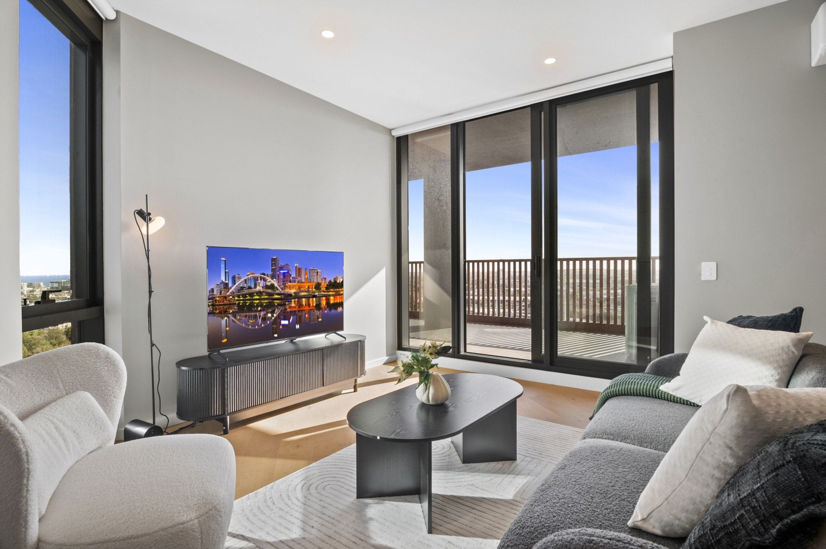 A modern living room with a flat-screen TV, a sofa, a coffee table, and a large window with a city view.