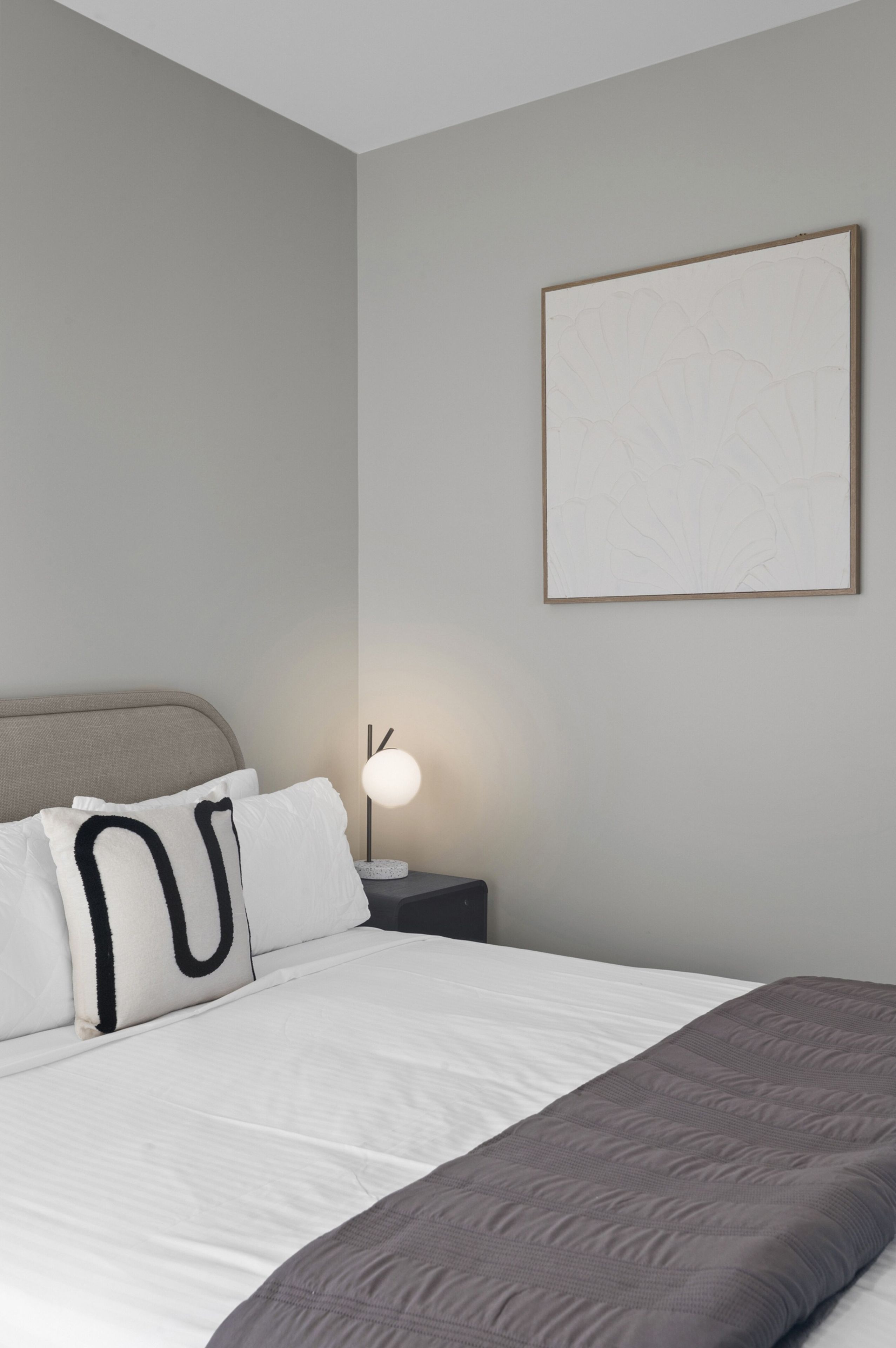 A bedroom with a bed, pillows, a bedside table with a lamp, and a framed picture on the wall.
