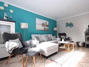 A modern living room with a teal accent wall, a grey sofa, a black armchair, and a small round table with a vase. - Holiday Apartment in Sylt With 2 Bedrooms (Sylt)
