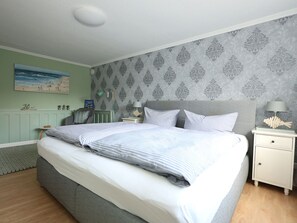 A neatly made bed with striped bedding, a bedside table with a lamp, and a wall with a patterned wallpaper. - Holiday Apartment in Sylt With 2 Bedrooms (Sylt)