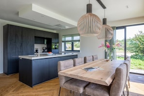 Eine moderne Küche mit einer zentralen Kochinsel, dunklen Schränken und einem Essbereich mit einem Holztisch und Stühlen.