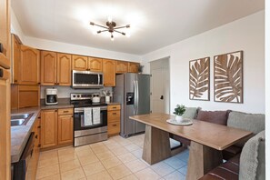 A modern kitchen with wooden cabinets, stainless steel appliances, a dining table, and decorative wall art.