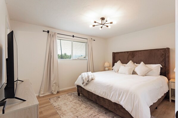 A bedroom with a bed, a nightstand, a lamp, a window with curtains, and a ceiling light fixture.