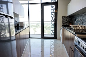 A modern kitchen with a large sliding glass door leading to a balcony, stainless steel appliances, and a tiled backsplash. - Vanilla Homes Premium 2BR in Masdar City (Abu Dhabi)