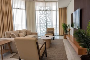 A modern living room with a sofa, armchair, coffee table, and a TV mounted on the wall. - Vanilla Homes Premium 2BR in Masdar City (Abu Dhabi)