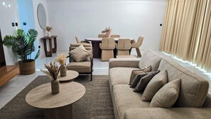 Een moderne woonkamer met een bank, salontafel en stoelen. In de achtergrond staat een eettafel met stoelen.