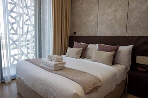 A hotel room with a large bed, a headboard with vertical slats, and a window with a geometric pattern. - Vanilla Homes Premium 2BR in Masdar City (Abu Dhabi)