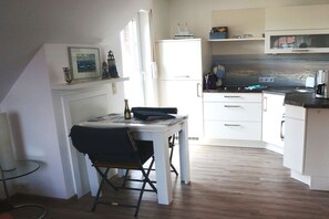 A compact kitchen with white cabinets, a small dining table, and a chair. - Baltrum at the "Kogge" house (Norden-Norddeich)