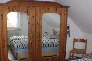 Een slaapkamer met een houten garderobe, een bed met gestreepte beddengoed, een stoel en een spiegel.