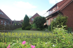 A residential area with brick houses, a metal fence, and a garden with various plants and flowers. - Baltrum at the "Kogge" house (Norden-Norddeich)