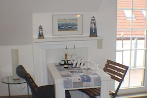 A dining area with a table set for two, a chair, a small table with a bottle, and a framed artwork above the table. - Baltrum at the "Kogge" house (Norden-Norddeich)