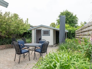 A patio with a round table and four chairs, a small shed, and a tall chimney. - Holiday Home in Koudekerke With Wi-fi (Koudekerke)