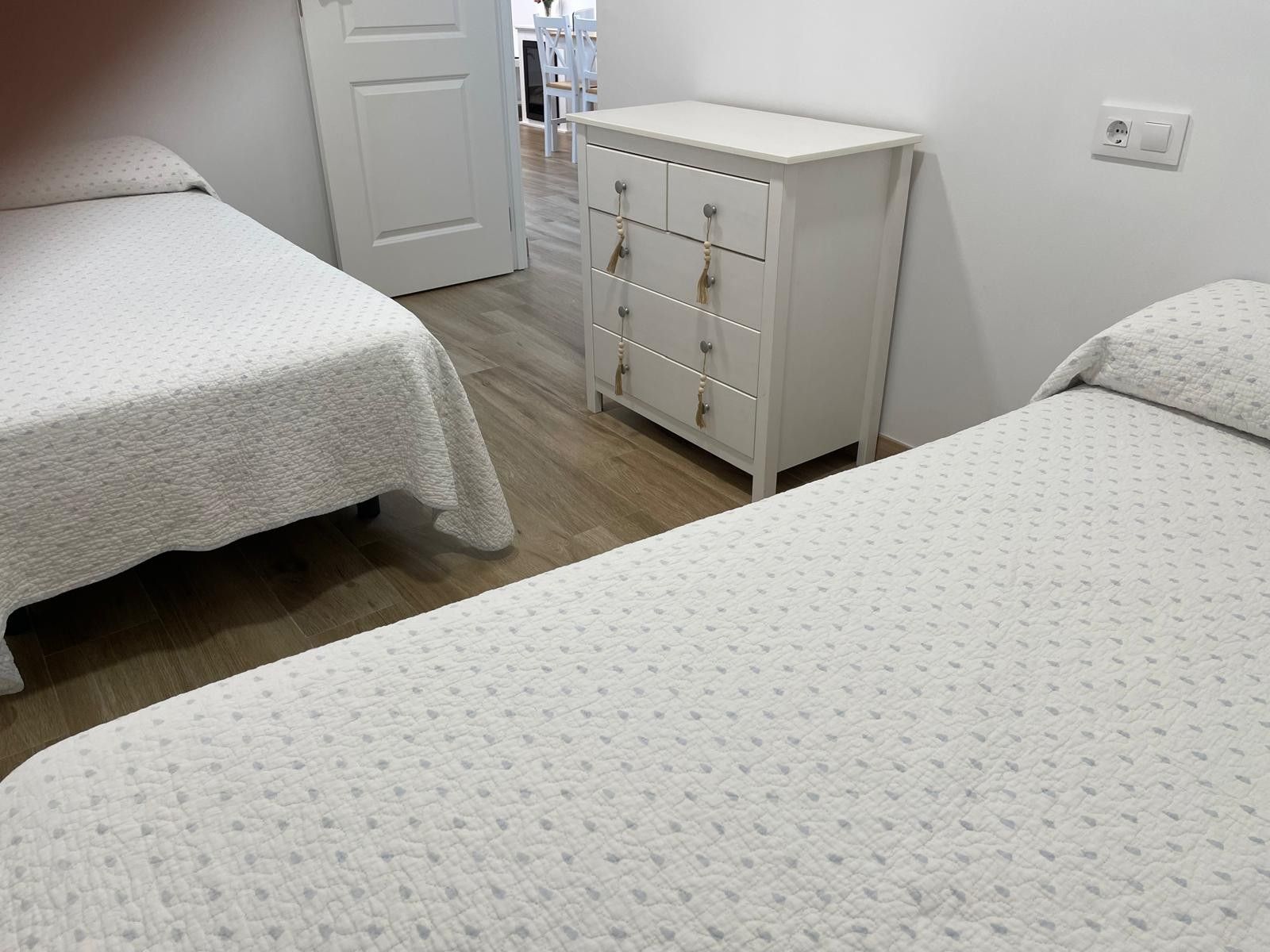 A bedroom with two beds, a white dresser with drawers, and a door leading to another room.