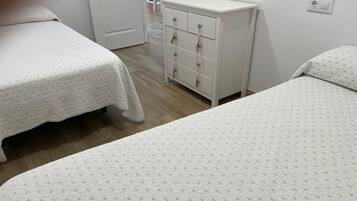 A bedroom with two beds, a white dresser with drawers, and a door leading to another room.