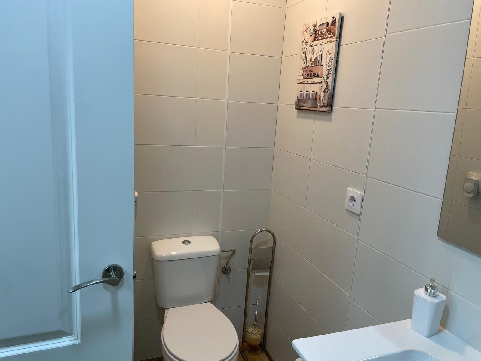 Ein Badezimmer mit Toilette, einer Haltestange, einem Wandregal mit Toilettenartikeln und einem weißen Waschbecken.