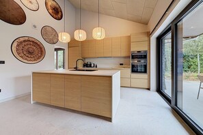 A modern kitchen with wooden cabinets, a central island, and built-in ovens. - Family retreat in Belgium with sauna (Rochefort)